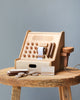 A Wooden Cash Register with buttons, a cash drawer, and a handheld scanner made from sustainably sourced wood, placed on a rustic wooden table against a gray background.