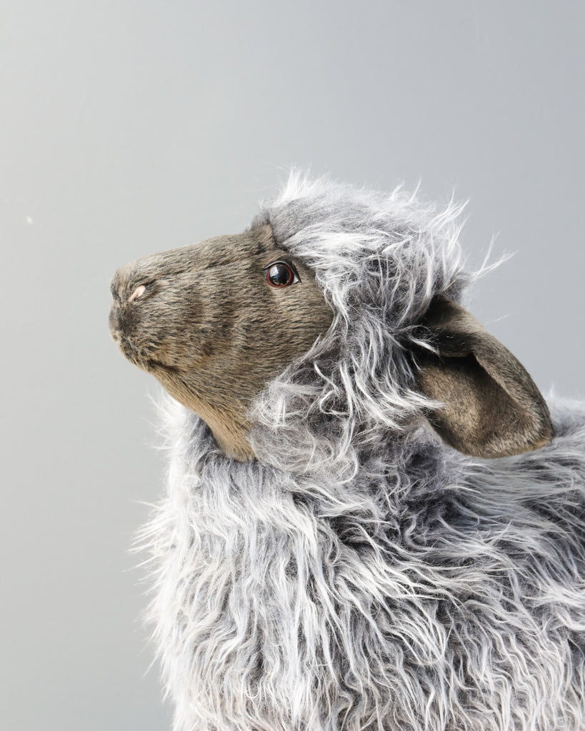 Profile view of a hand-sewn plush Sheep Stuffed Animal with fluffy gray fur against a plain light background, showcasing detailed features and textured fur.