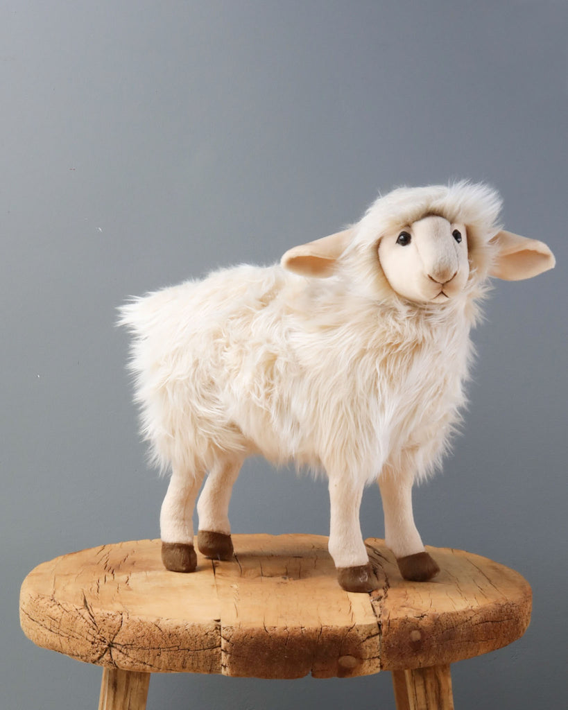 A handmade Sheep Stuffed Animal with soft white fur standing on a circular wooden stool against a plain grey background.
