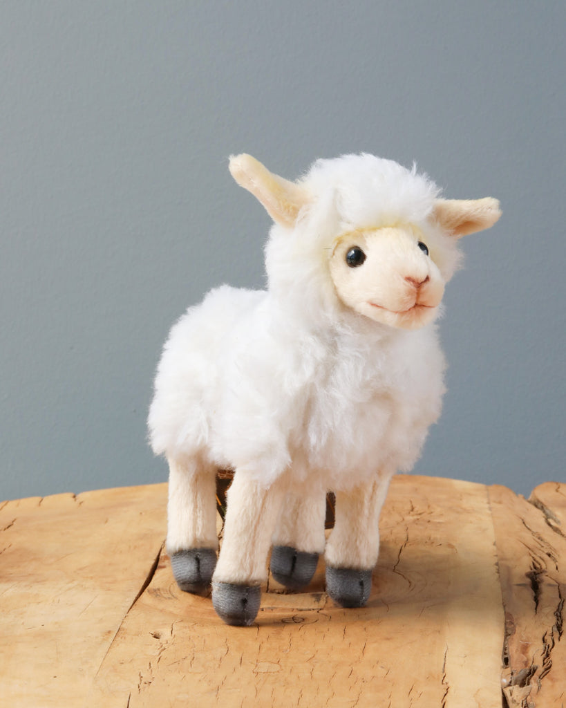 A handmade Sheep Stuffed Animal with a fluffy white coat and soft gray hooves, standing on a circular wooden stump against a light blue background.