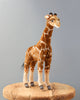 A Giraffe Stuffed Animal standing on a circular wooden base against a plain grey background, showcasing detailed patterns and lifelike eyes, crafted from high quality man-made materials.