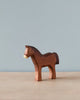 A Handmade Holzwald Dark Brown Horse figurine, crafted from high-quality materials, stands against a soft blue backdrop, featuring intricately carved details and a rich brown color with white accents on the mane.