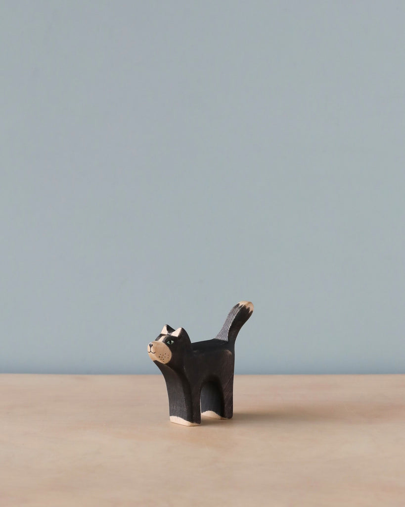 A small Handmade Holzwald Black Cat figurine with white details on its face and tail, standing against a plain, light blue background. This piece is part of a collection of sustainable toys.