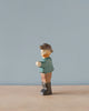 A high-quality Handmade Holzwald Farmer figurine of a person wearing a hat, green shirt, and brown pants stands against a plain blue background. The figurine is depicted in a walking pose.