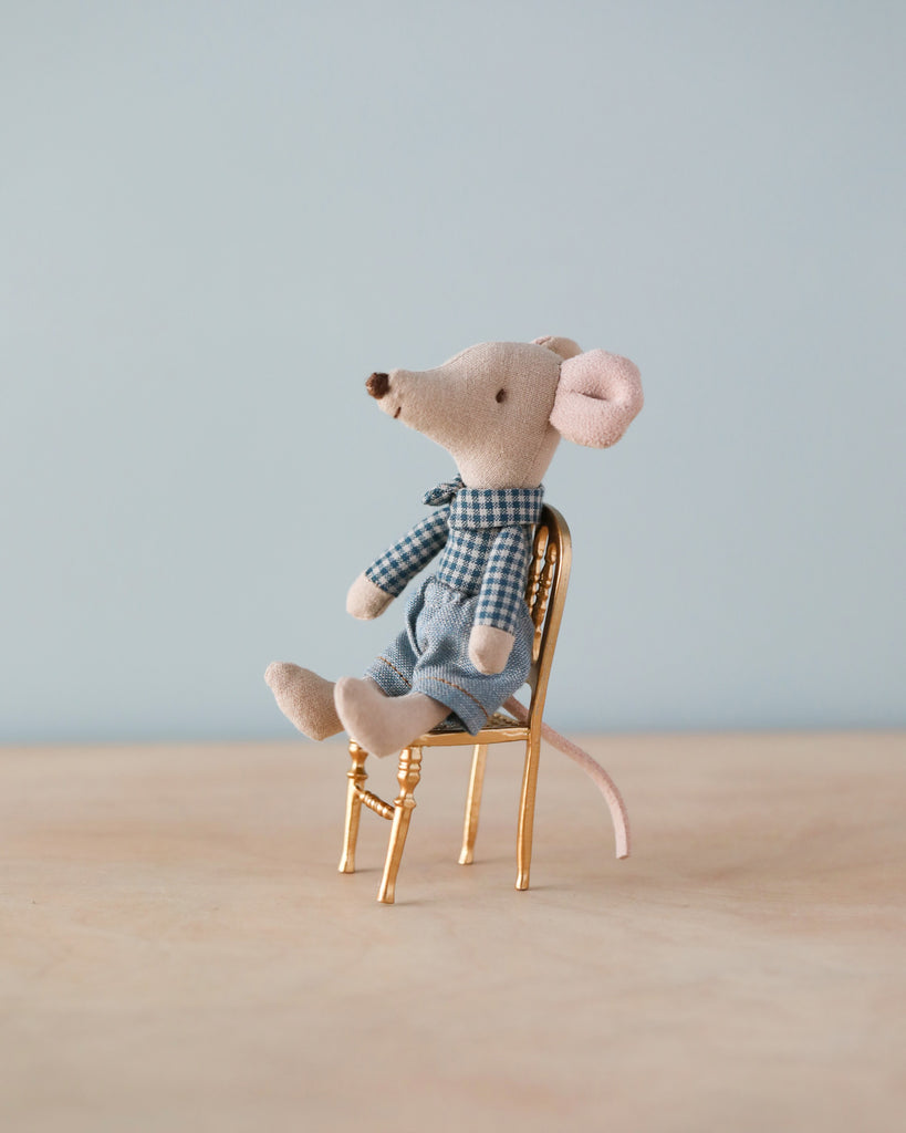Beige cloth mouse with blue plants and lea and white checkered shirt sitting on gold metal chair. Natural color counter and light blue background.