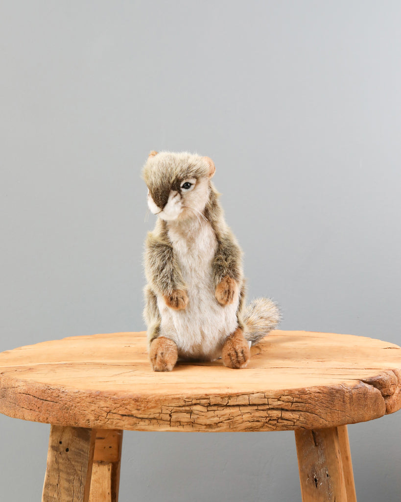 A Standing Squirrel Stuffed Animal, artisan hand-sewn and sitting on a round wooden table against a plain grey background, is depicted with realistic fur textures and lifelike eyes.
