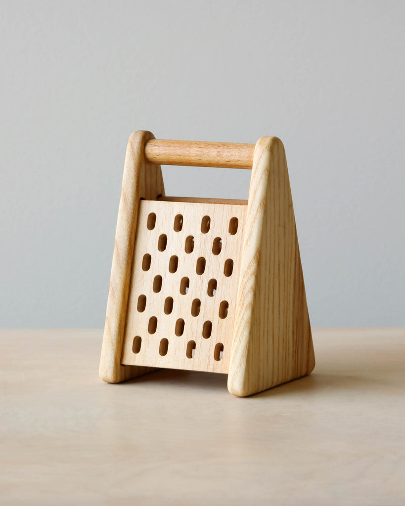 Wooden pretend play cheese grater. Natural color counter and light blue background.