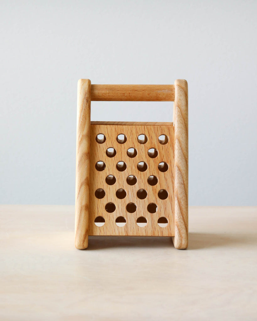 Front side of pretend play wooden grater. Light blue background and natural color counter.