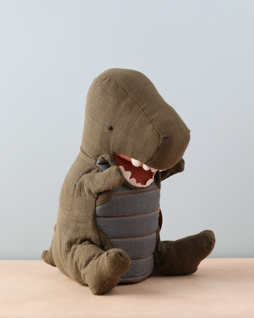 Green dinosaur puppet sitting on natural color counter. Light blue background.