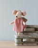 A Maileg Angel Mouse in Metal Suitcase wearing a light pink dress with a golden halo and wings stands atop a stack of decorative suitcases. The mint colored suitcase, adorned with star patterns and glittery straps, is set against a light blue background.