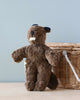 A Senger Naturwelt Stuffed Animal - Baby Beaver, handmade in Germany with a small white patch on its mouth, sits against a wicker basket on a wooden surface, with a light blue backdrop.