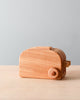 The Handmade Wooden Toaster has a simplistic design on a grey tabletop against a pale blue background. The toaster has a round knob on the side and a slot on top for bread.