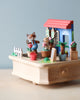 A Wooden Fox Gardener Music Box from Wooderful Life, featuring animal figurines, a house, plants in pots, a fence, and gardening tools on a simple wooden base. The setting is against a