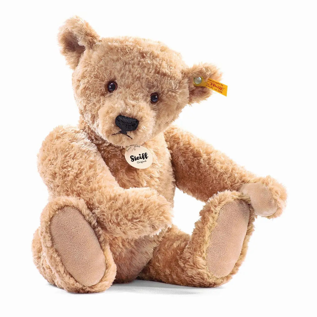 A handmade Steiff Elmar Teddy Bear with a fluffy golden-brown fur, sitting upright and displaying its iconic Button in Ear and a chest tag with the brand name.