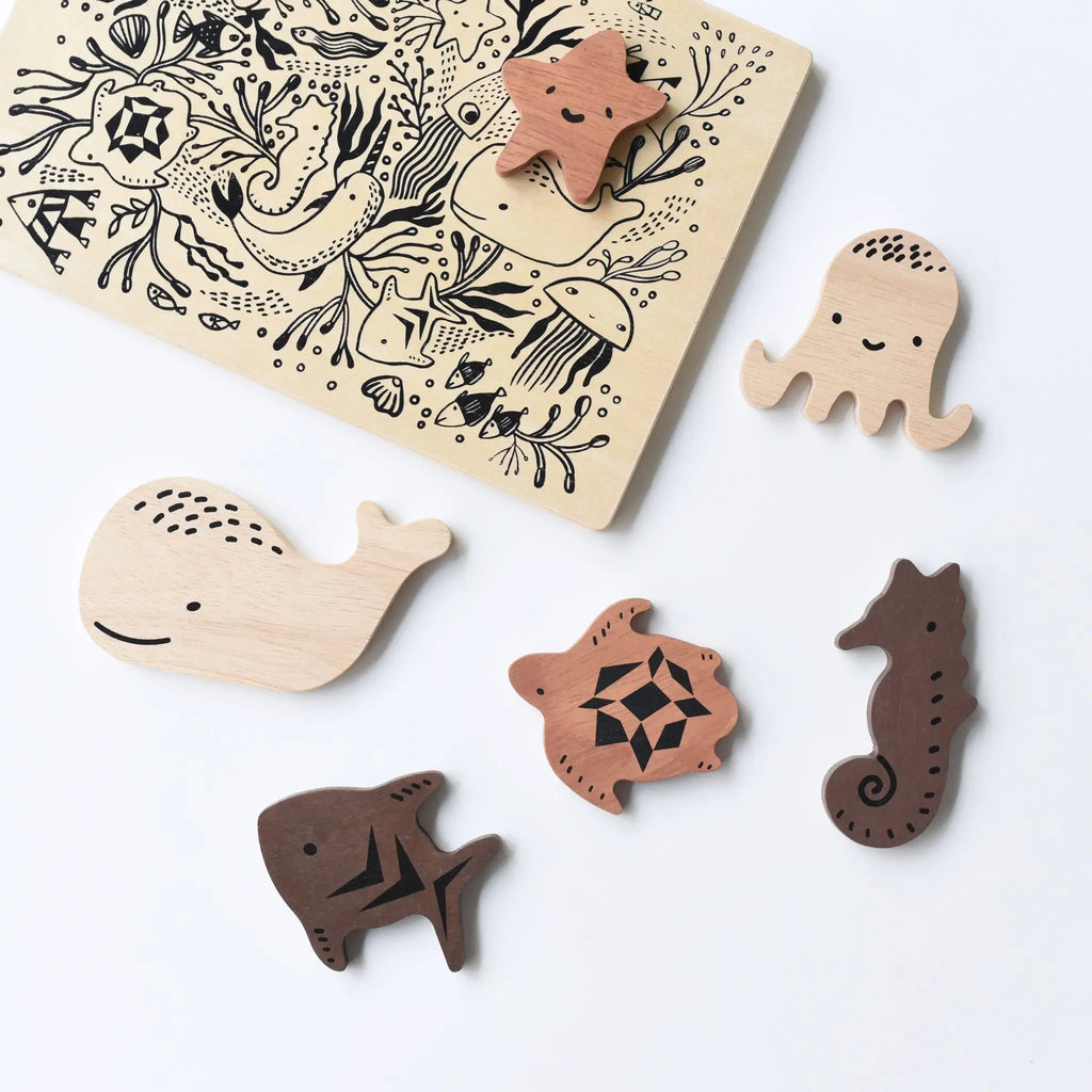 A flatlay of the Wooden Tray Puzzle - Ocean Animals set featuring sea creature pieces including a whale, shark, starfish, octopus, and seahorse, next to a puzzle board with intricate ocean-themed line