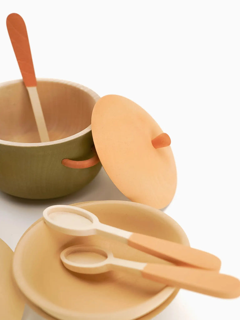 A minimalist set of eco-friendly, non-toxic Handmade Wooden Kitchen Essentials - Herbal featuring a green bowl with a wooden spoon, an orange lid, and beige plates with utensils against a white background.