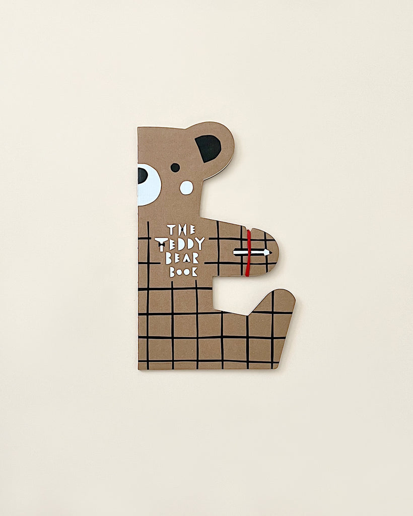 A puzzle piece shaped like a teddy bear featuring a grid design and part of a book title "The Teddy Bear Drawing Book" in stylized text. The background is decorated with drawings of teddy