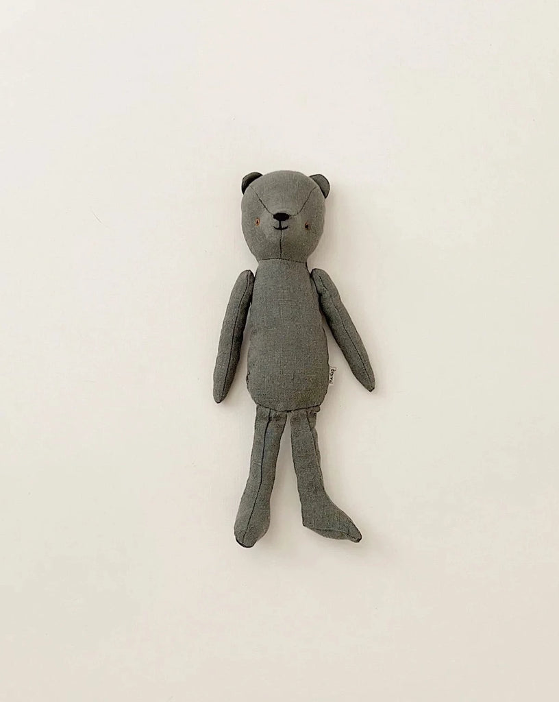 A Maileg Teddy Dad made of soft linen in a grey fabric is laid out on a plain white surface. The bear has simple stitched facial features, offering a vintage look with its minimalist design and long limbs.