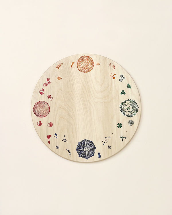A wooden plate with artistic floral and geometric designs painted in various colors around the rim, set against a plain white background, resembling elements of the Grapat Seasonal Platform.