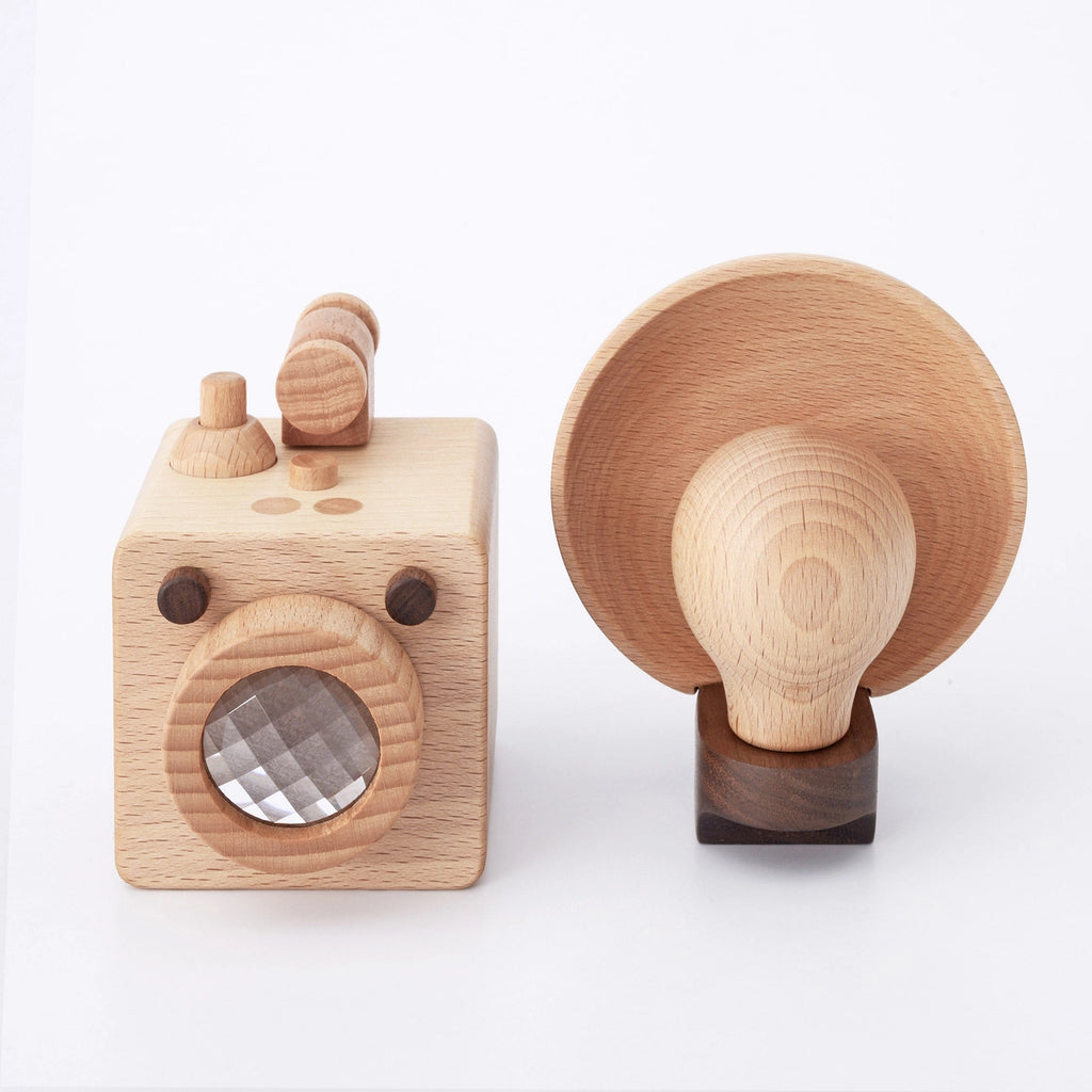 Two wooden desk accessories on a white background: the Father's Factory Wooden Light Bulb Camera keep-sake piece on the left, and a mushroom-shaped lamp base on the right, both crafted from light-colored wood.