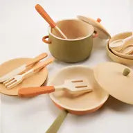 Assorted biodegradable handmade wooden kitchen essentials including plates, utensils, and a pot with wooden handles on a light background.
