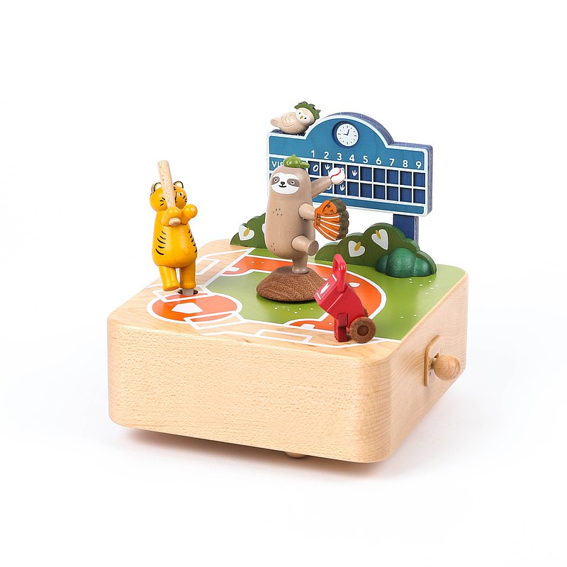 A colorful Baseball Music Box featuring a whimsical forest theme with a bear, trees, a bee, a squirrel, and a musical score. A small crank on the side is used to