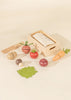 Sliceable wooden vegetable toys laying flat with a wooden crate and wooden knife.