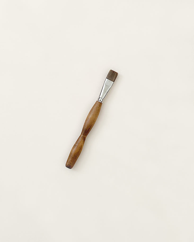 A single Stockmar Paint Brush - Flat Tip with a wooden handle and metal ferrule, positioned centrally on a plain, light-colored background.