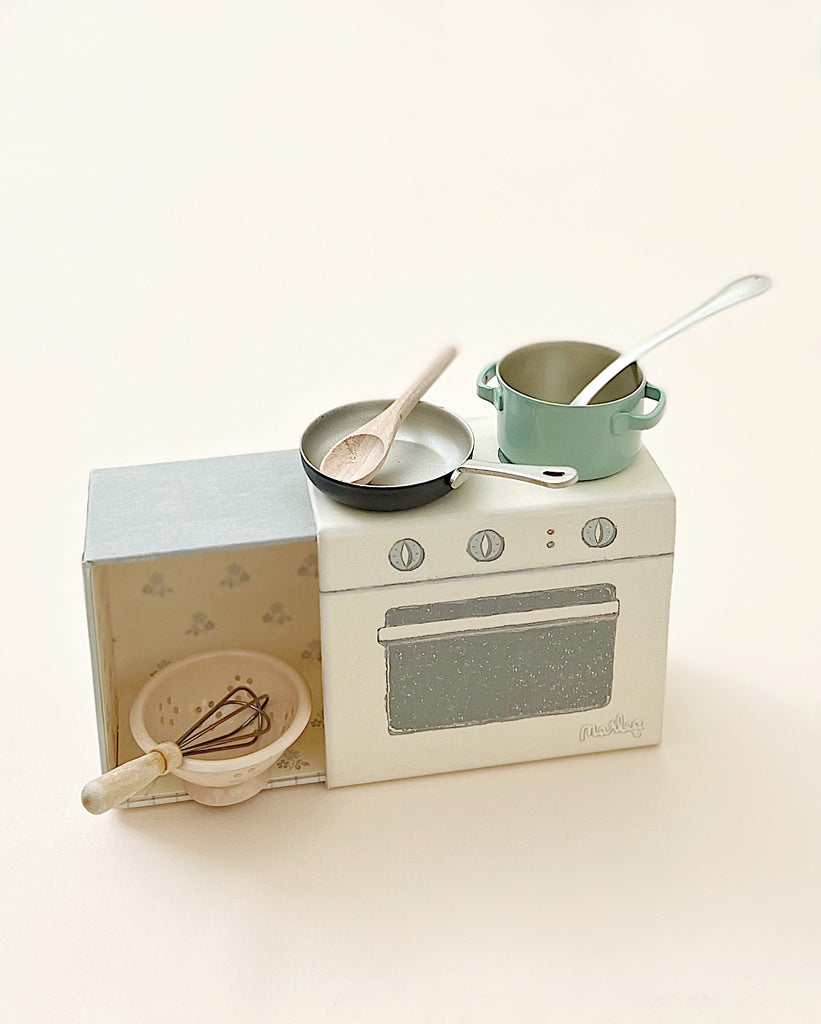 A Maileg Cooking Set featuring a playful stove, oven, and several utensils including a whisk, a saucepan, and a spoon. The set is displayed against a plain, light background.