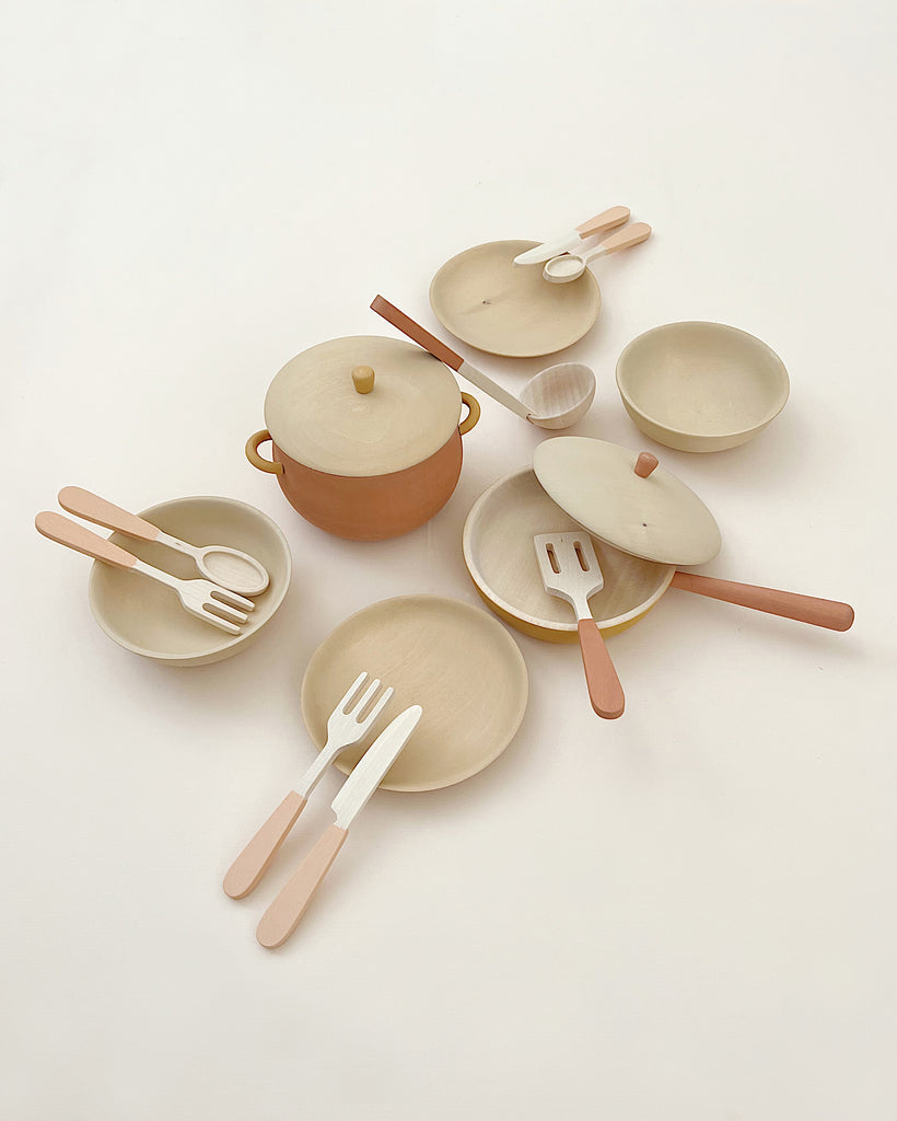 A set of minimalistic, wooden kitchen utensils and dishes, including plates, bowls, a pot with a lid, and various forks, spoons, and spatulas—each piece of this Handmade Wooden Kitchen Essentials - Flower is carefully arranged in an aesthetically pleasing manner on a light-colored surface.
