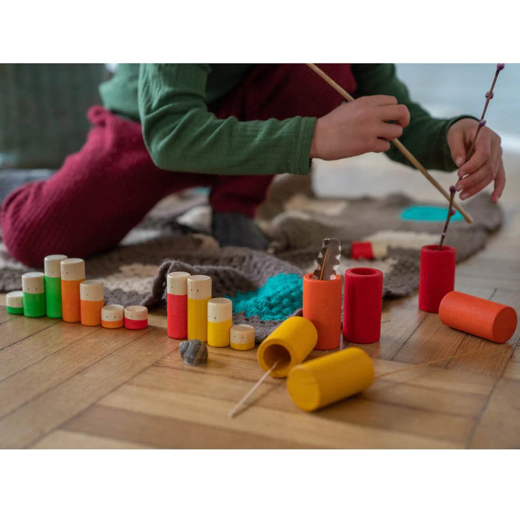A child in colorful clothing sits on the floor, using sticks to engage with the Grapat LA Non Basic Colors play set 36 pcs scattered around them.
