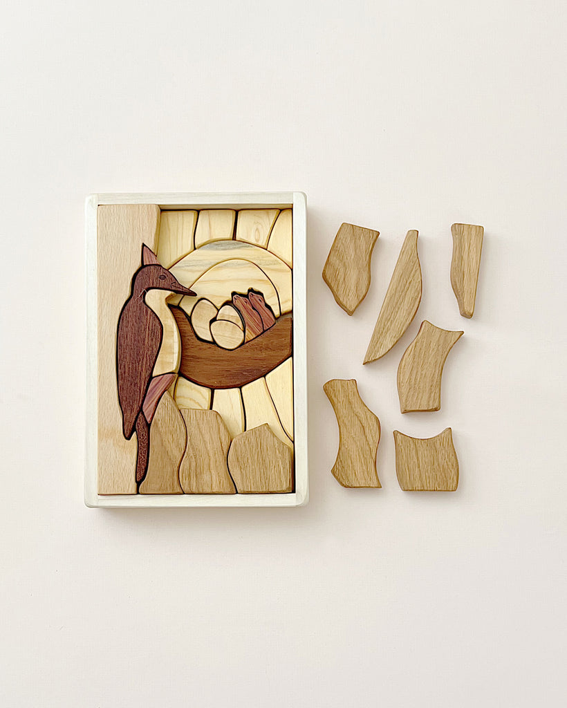 A Handmade Double Layer Wooden Puzzle - The Nest on a light background, featuring a partially completed image of bird nesting habitats, with several puzzle pieces laid out beside it.