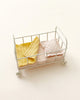 A Maileg Micro Cot filled with neatly folded towels, a cozy cot bed cushion, and micro-sized friends on a plain light background.