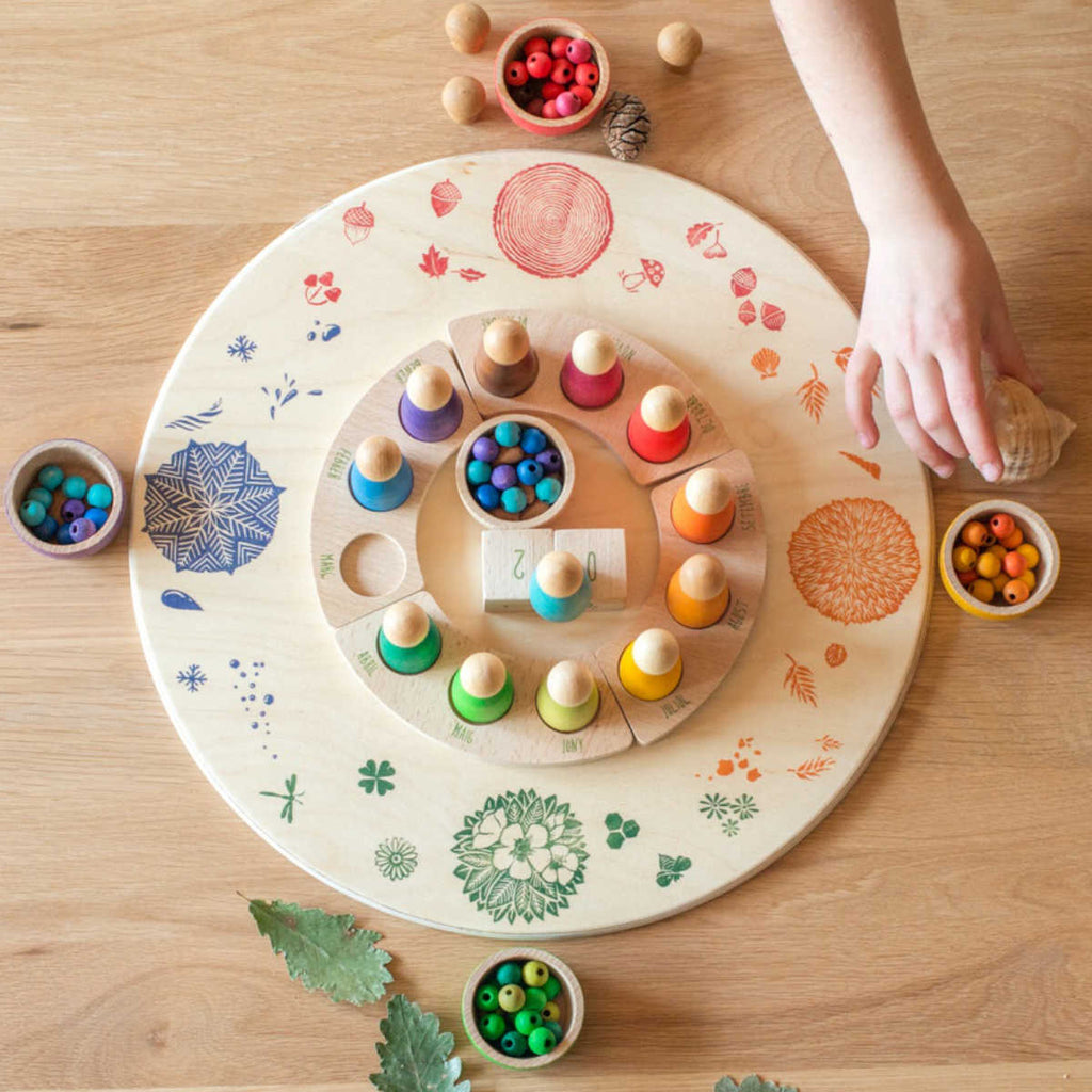 A child's hand reaching out to a Grapat Seasonal Platform, which features circles filled with various colored beads, on a wooden platform.