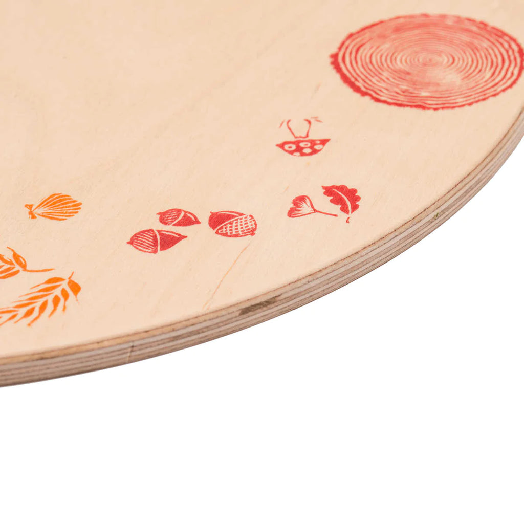 Close-up view of a Grapat Seasonal Platform board with red stamped designs including a tree ring, leaves, and small abstract shapes, slightly angled to show the board's edge.