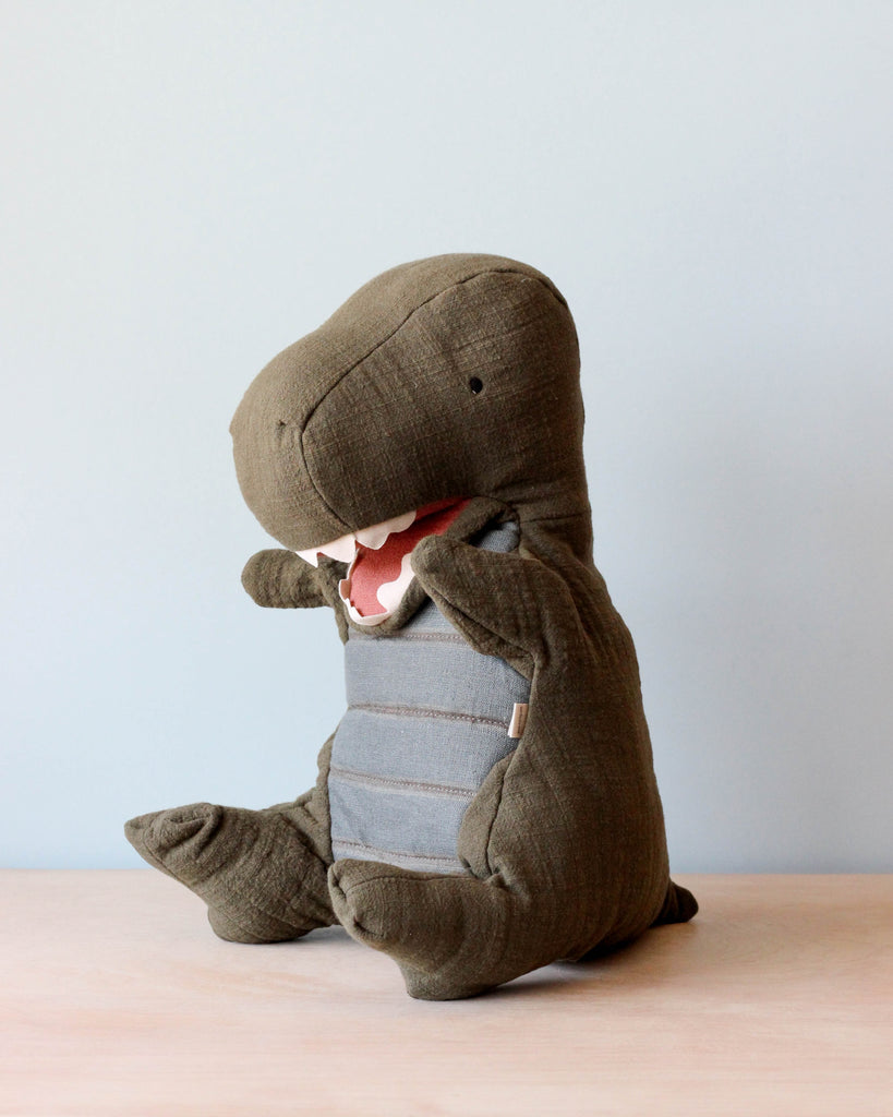 Green dinosaur puppet sitting on natural color counter. Light blue background.
