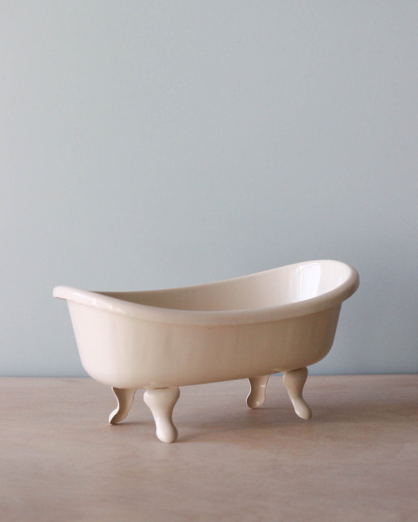 A small ceramic Maileg Mini Bathtub, positioned on a wooden surface against a light blue background.