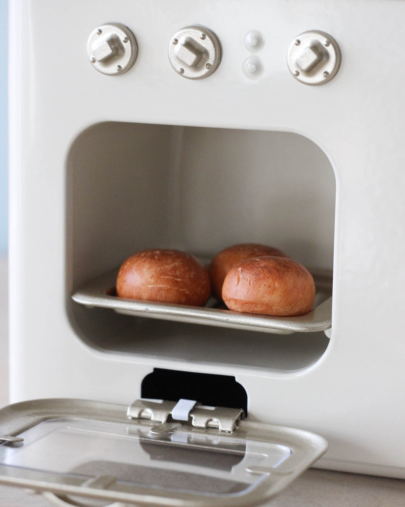 Two freshly baked buns resting on a shelf inside a vintage white bread box with round knobs and an open hatch, perfect for a Maileg Mini Kitchen.