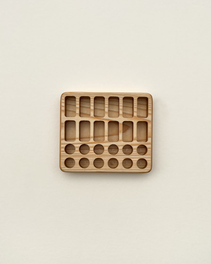 A Crayon Tray For Stockmar -12 x 12 Slots with various shaped holes for educational purposes, now also serving as a crayon holder, placed on a plain beige background.