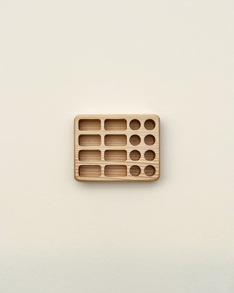 A minimalist image showcasing a Crayon Tray For Stockmar - 8 x 8 Slots with various sized compartments, each containing a different number of cylindrical Linden wood pieces, arranged on an off-white background.