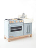 A Milton & Goose wooden play kitchen painted in light blue, featuring a stove, oven, and sink with wooden knobs. This Amish crafted play kitchen is set against a plain white background.