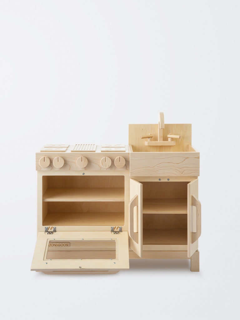 An Milton & Goose Wooden Play Kitchen - Made in USA, featuring a sink, stovetop, and storage cabinets, all made of sustainable Baltic birch wood and designed to look like a miniature real
