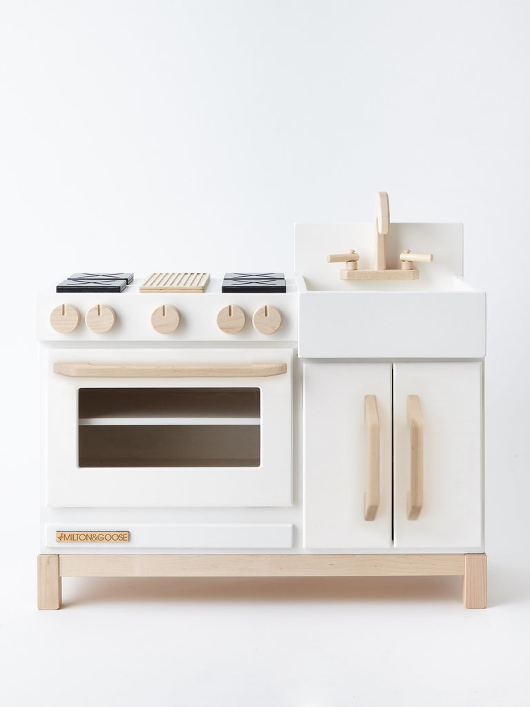 A Milton & Goose Wooden Play Kitchen - Made in USA featuring a white and natural wood color scheme, crafted from sustainable Baltic birch, with a stove, oven, and sink.