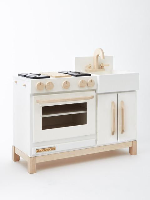 A Milton & Goose wooden play kitchen featuring a stove with knobs, an oven with a viewing window, and a small sink, all designed in white with sustainable Baltic birch accents.