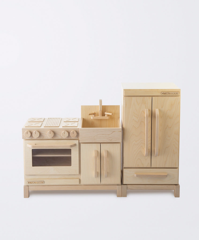 A wooden toy kitchen set featuring a stove, oven, sink, and Milton & Goose Pretend Refrigerator - Made in USA, all crafted in natural wood with detailed knobs and handles.