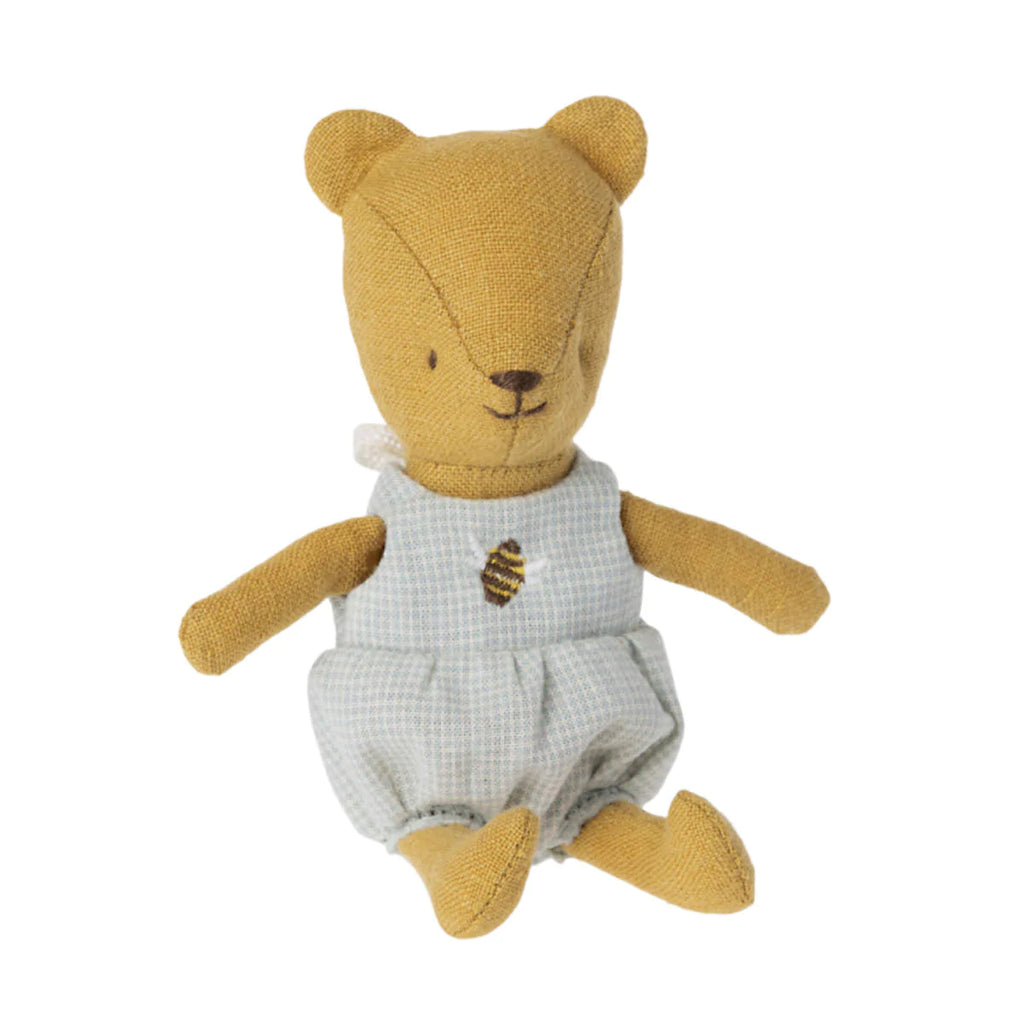 A Maileg Teddy Baby with a yellow head and limbs, wearing blue and white checkered overalls with a bee patch, sitting against a white background.