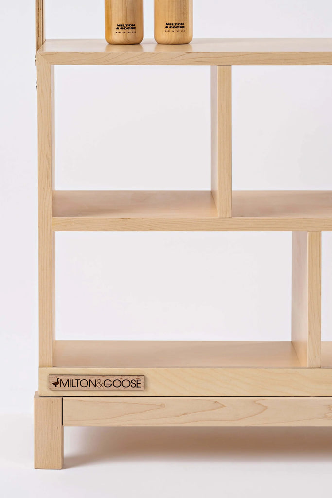 A minimalist Milton & Goose Market Stand with three shelves displaying clean lines and a small logo "milton & goose" on the bottom side. The shelves are empty except for two matching heirloom quality wooden containers.