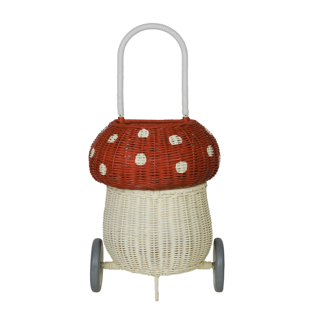 A whimsical Olli Ella Rattan Mushroom Luggy - Red on wheels designed to look like a mushroom, featuring a red top with white polka dots and a white base, complete with a sturdy handle.