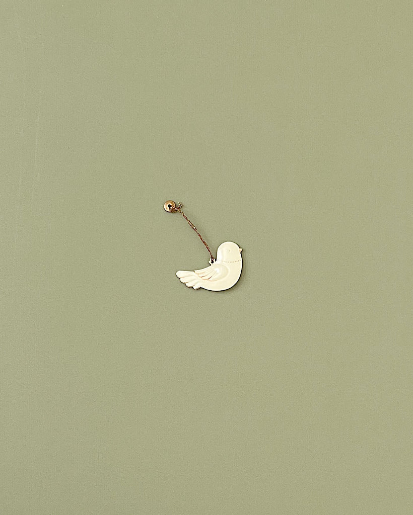 A Maileg Metal Bird Ornament, reminiscent of Maileg ornaments, is suspended by a thin string from a small mounted pin against a plain, light green background. The white bird, with minimal details, appears to be in mid-flight—an elegant touch for any home decoration or Christmas tree.