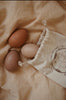 Canvas bag. 3 wooden egg shakers. Photographed on beige fabric. 